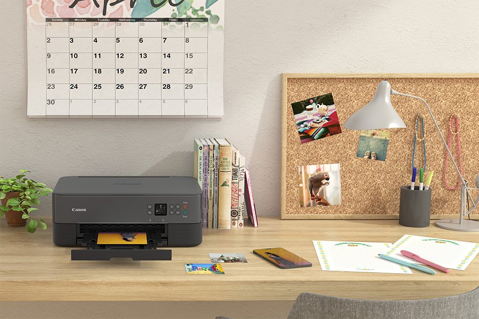 A Canon home and creative printer on a desk with other work-related essentials. 