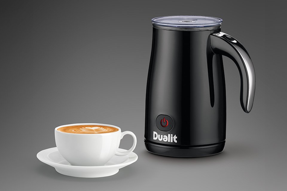 A Dualit 1 cup milk frother with a cup of coffee next to it. 