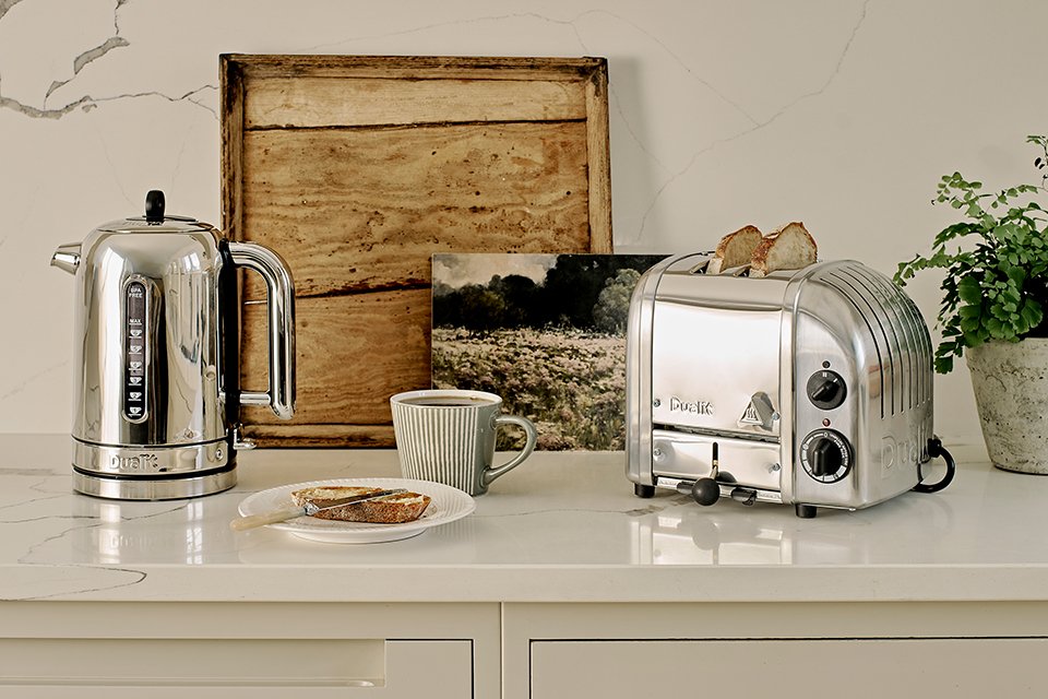 A Dualit stainless steel Classic toaster and kettle with other things on a white kitchen counter. 