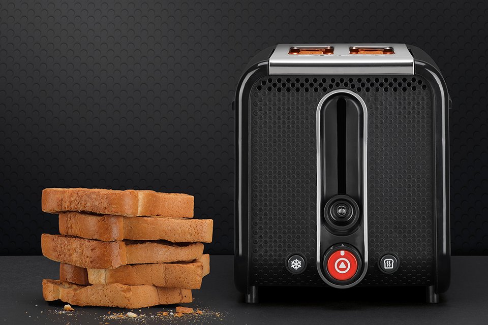 A Black Dualit Studio 2 slot toaster with some slices of toasted bread next to it. 