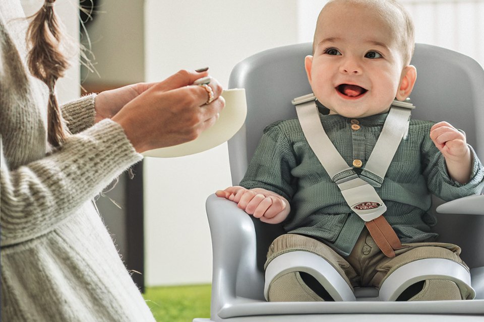 A mother feeding her baby in a Chicco Zest Folding Highchair - Moon Grey.