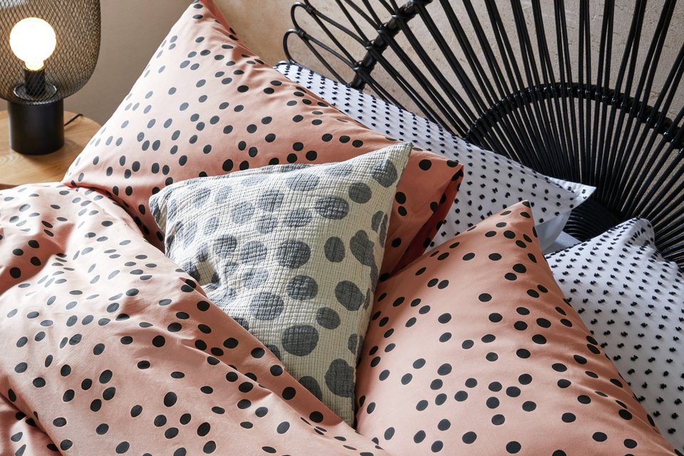 Pink bedding with black dalmatian spots on a bed with black headboard.
