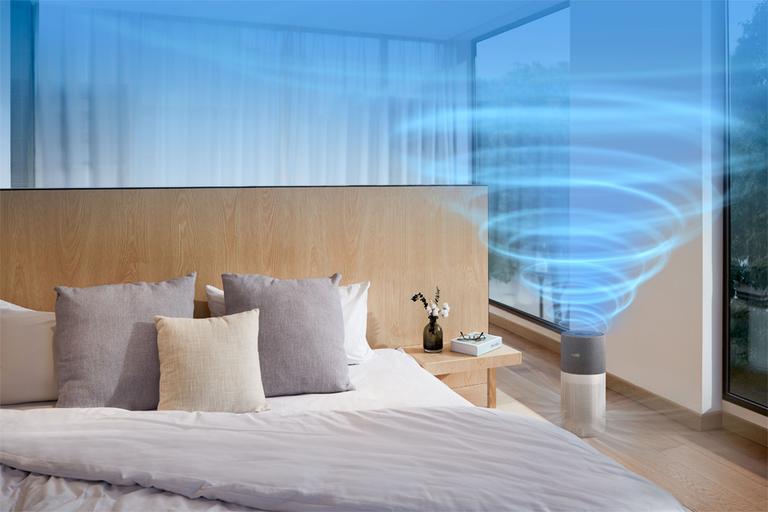 Image shows a Philips air purifier in use by the side of a bed, with blue waves to show the movement of air