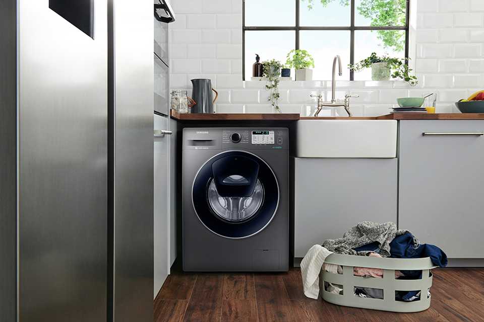 A graphite Samsung washing machine in a kitchen with a laundry basket in front.