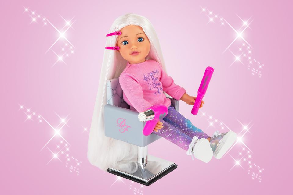 A DesignaFriend doll sitting on a tiny chair and holding a hair-dryer and a brush.