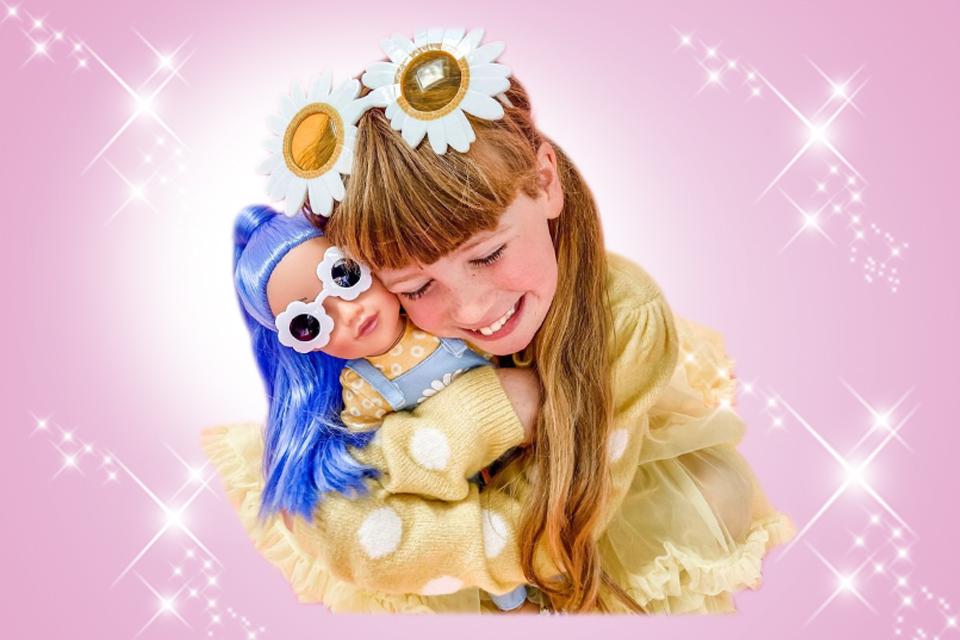 A young girl hugging a DesignaFriend doll with blue hair and sporty sunglasses.