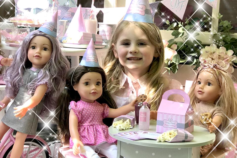 A young girl with 3 DesignaFriend dolls and party decorations placed on a tabletop.