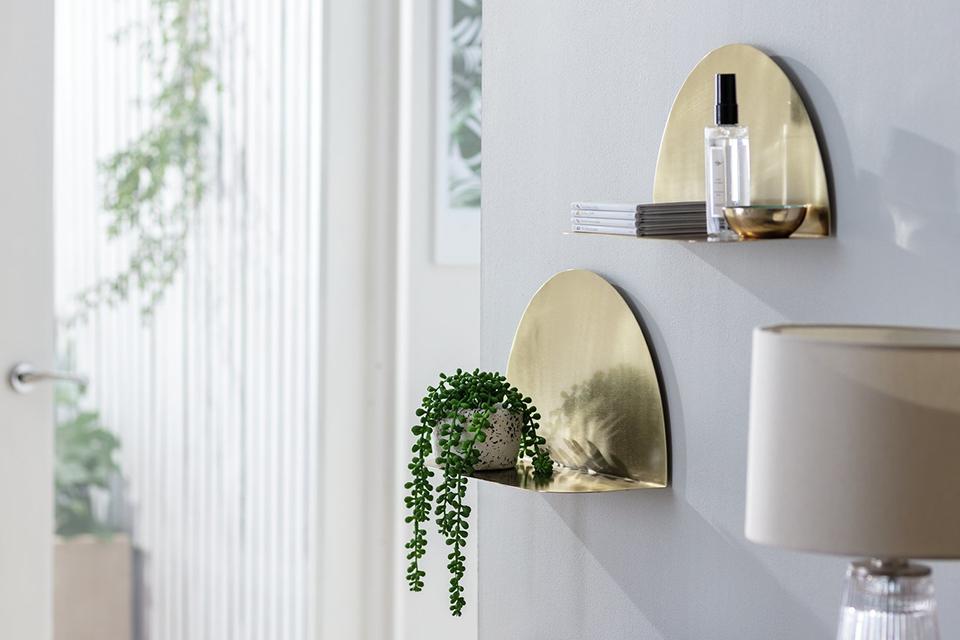 Two gold finish metal arched wall shelves with a plant.