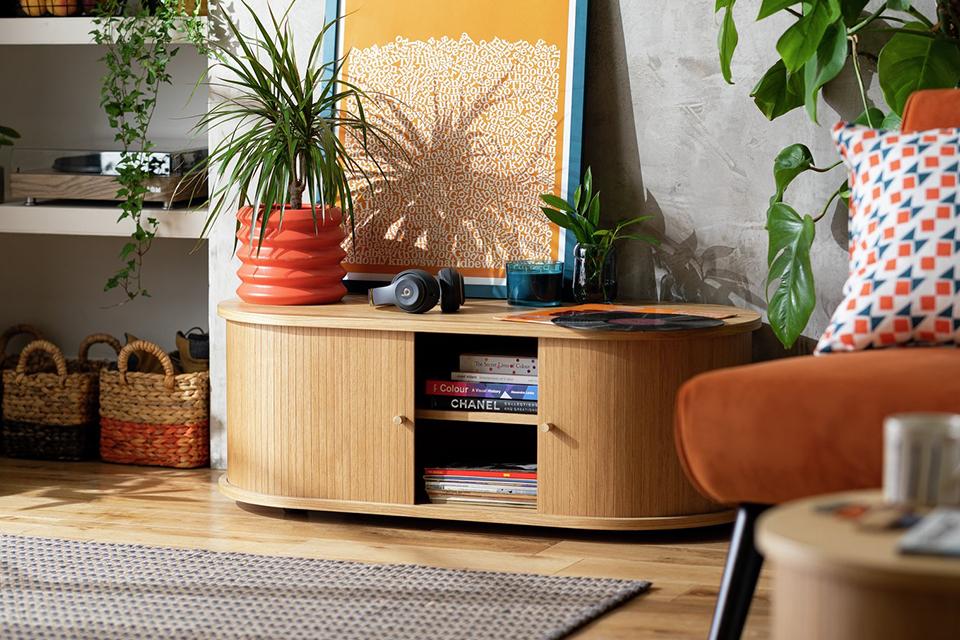 A wooden finish cabinet in a living room with an indoor plant, headsets and a wall art frame placed on it. 