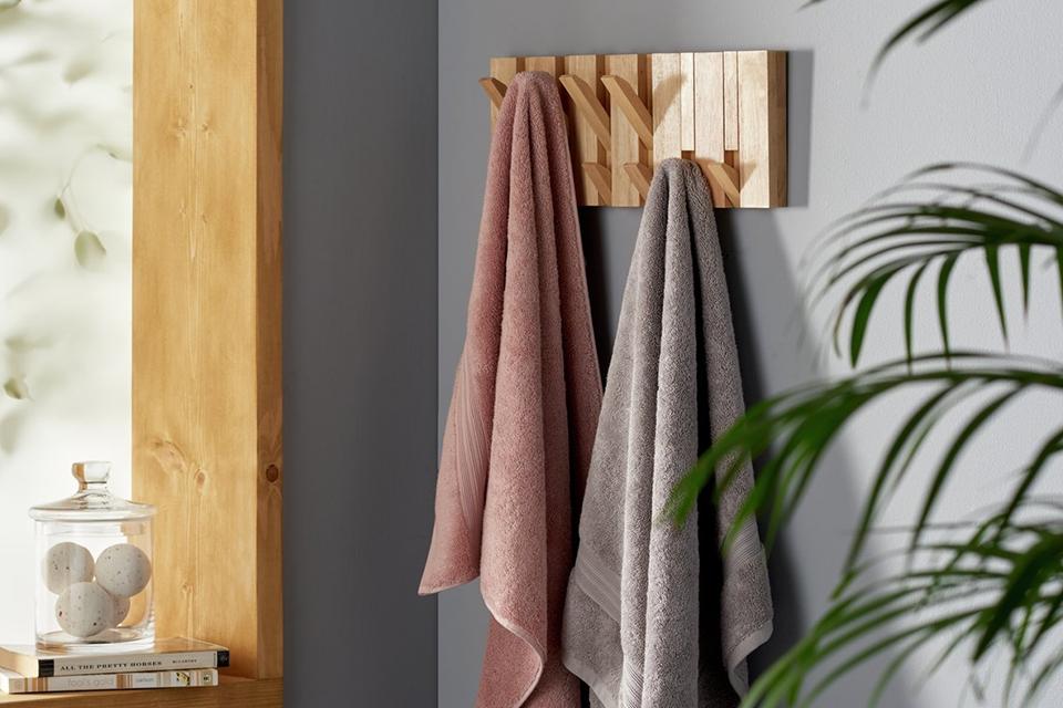 Wooden wall hook storage with pink and grey hand towels in a grey bathroom.