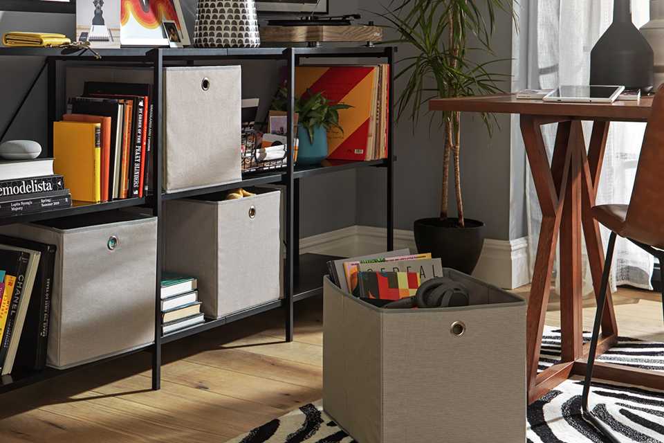 A set of 4 woven linen square plus boxes in grey placed on a metal wired cube storage shelf  in black with books and other home accessories.