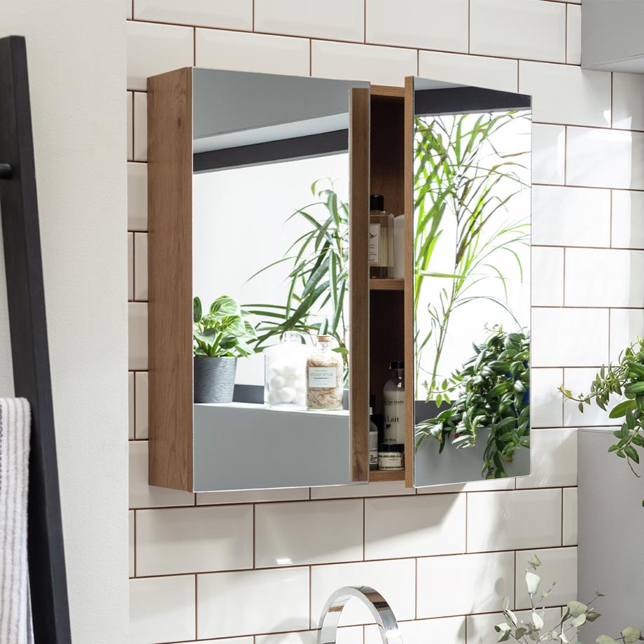 A bathroom mirror with storage shelf above a sink and wooden cabinet. 