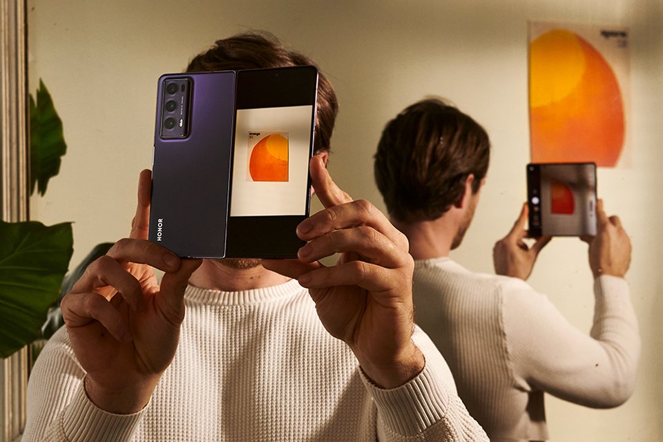 A man taking a photograph of a painting on a wall with his HONOR Magic V2 foldable phone.