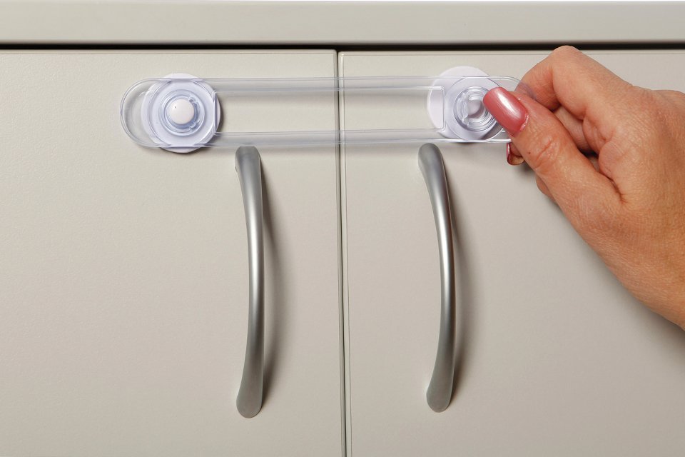 A woman's hand securing Dreambaby safety lock on a cabinet.