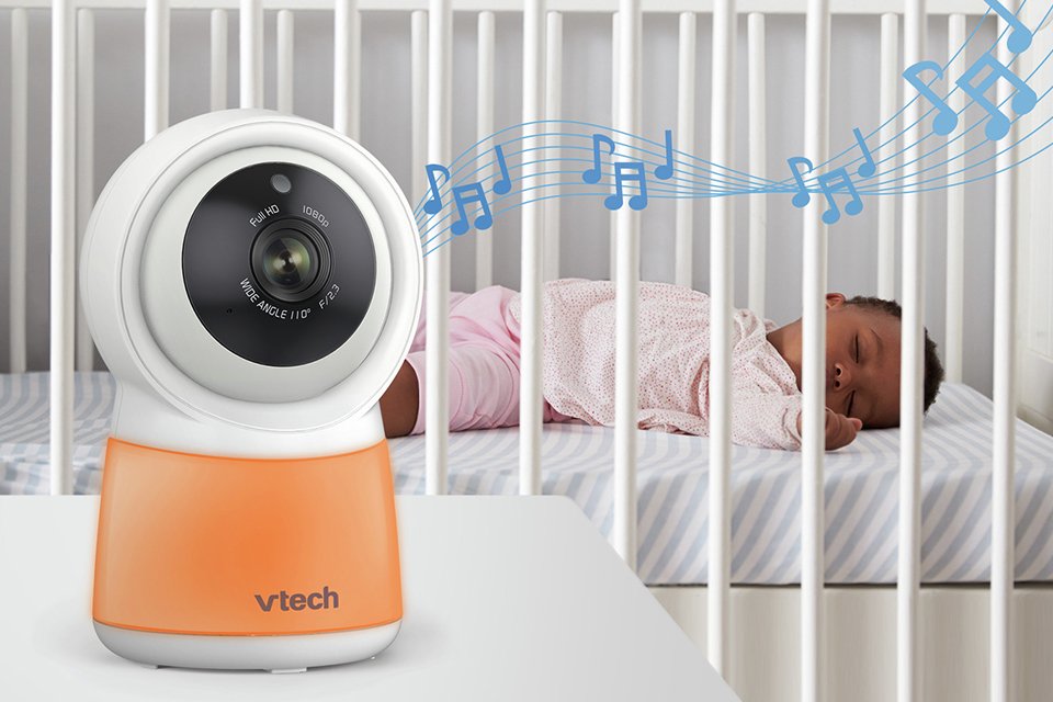 A VTech RM5755 5inch HD Smart Video Baby Monitor next to a baby in a cot bed.