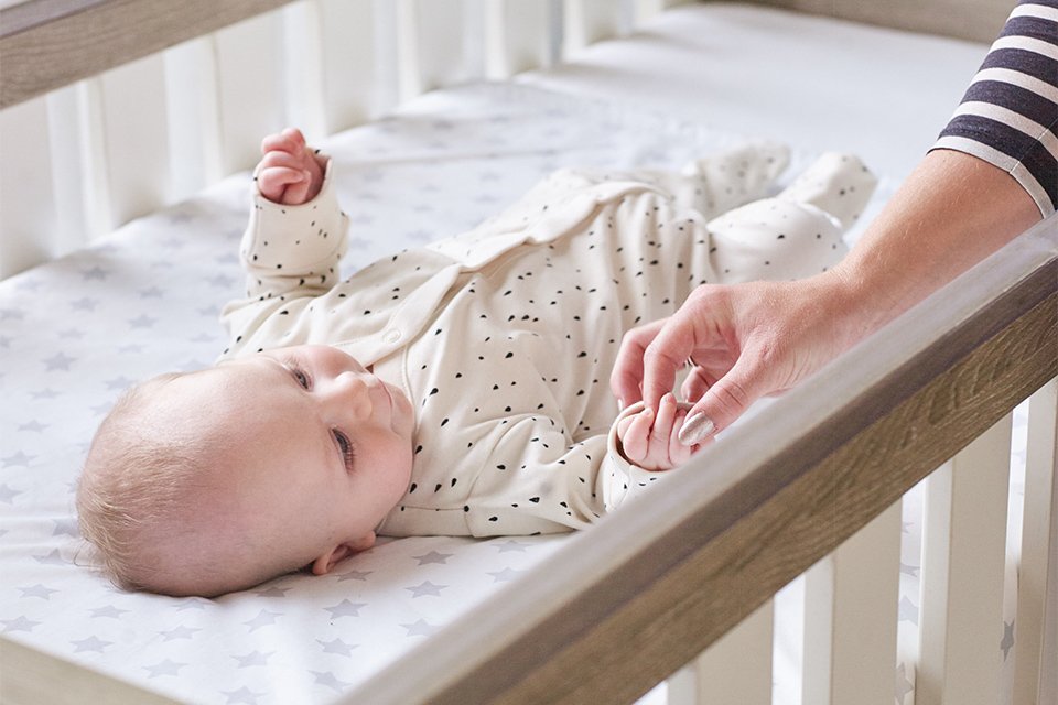A mother playing with a baby while the baby is sleeping in a cot bed.