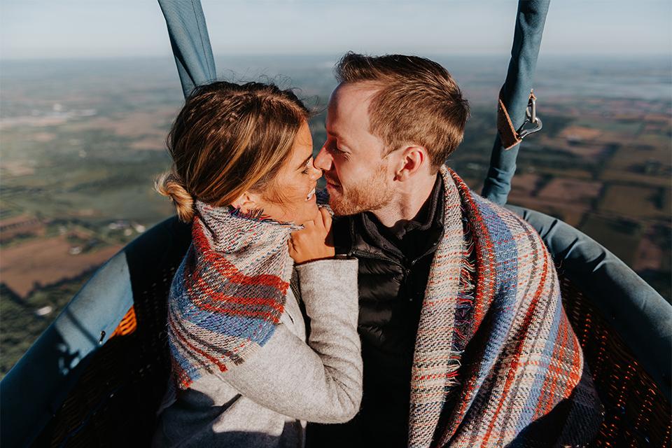 Two people kissing whilst on a balloon ride.