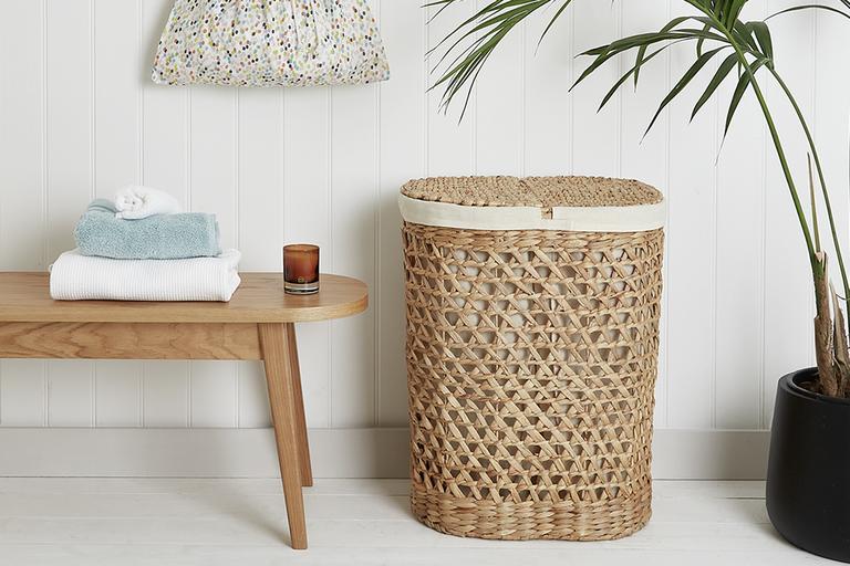 Image of a wicker laundry basket next to a wooden bench and plant.
