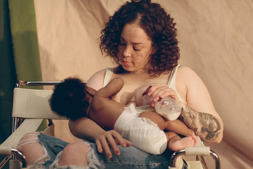 Image shows a woman breastfeeding at the same time as expressing milk with the Tommee Tippee manual breast pump.