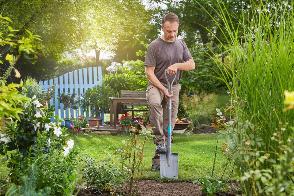 A man uses a GARDENA One-piece tools spade to dig into a garden bed.