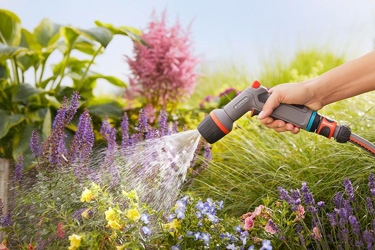 A hose with a GARDENA EcoPulse Spray nozzle attached is used to water some plants.