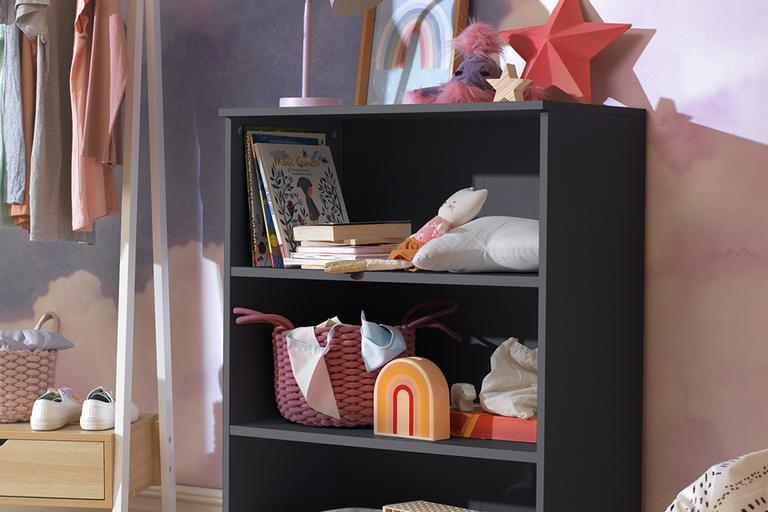 A grey kid's bookcase with books, toys and a pink storage trunk in it. 