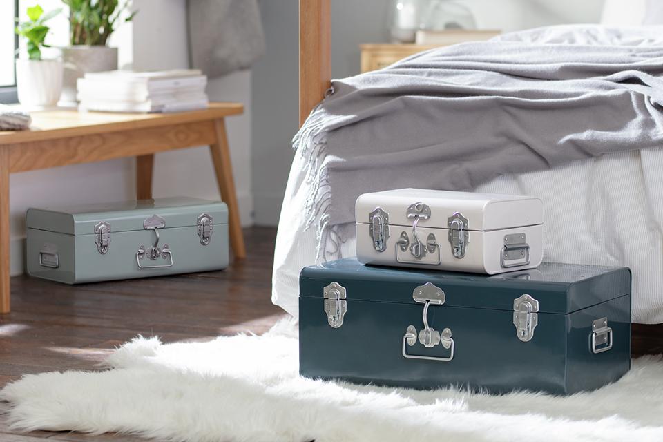 A set of 3 storage trunks in grey, blue and white placed in a bedroom on a fur rug. 