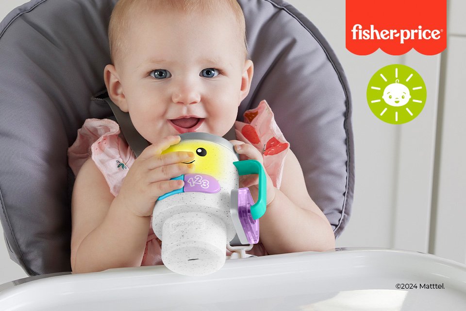A baby holding a Fisher-Price sipper while smiling at the camera.