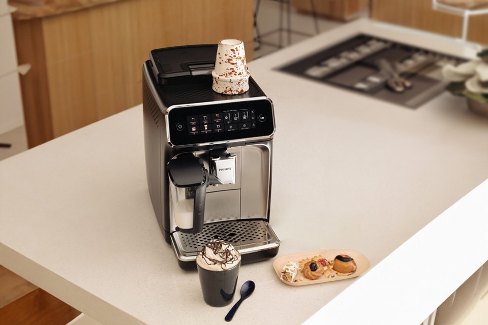 A black Philips bean to cup coffee machine on kitchen counter with a cup of coffee and cookies next to it.