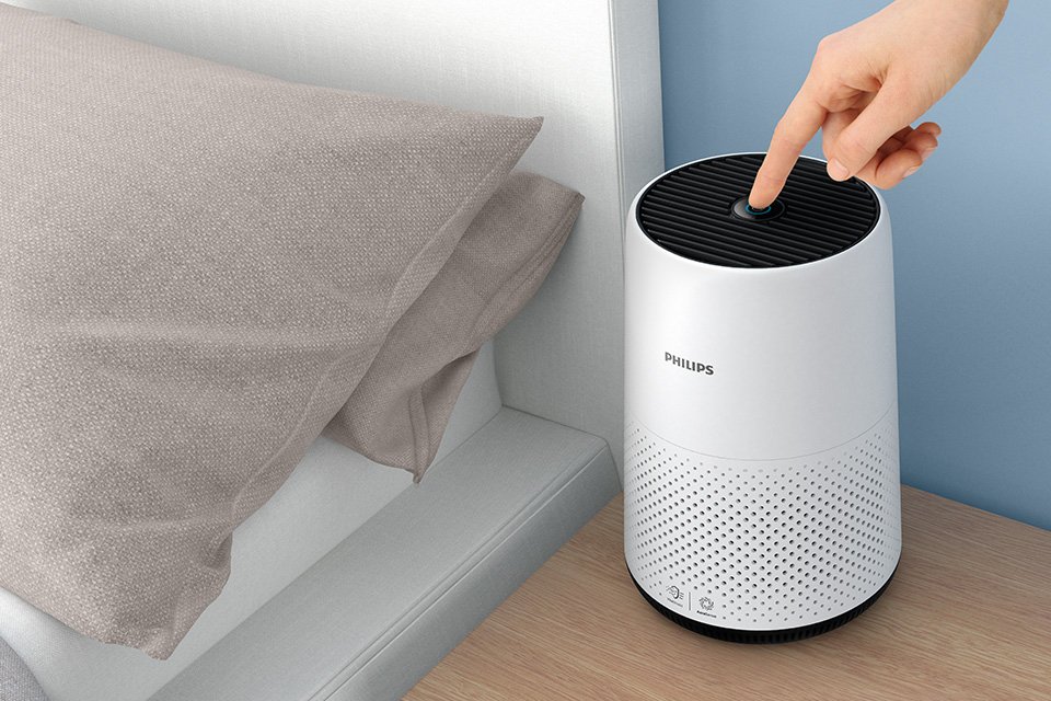 A finger switching on a white Philips 800 Series Air Purifier placed on a beside table.