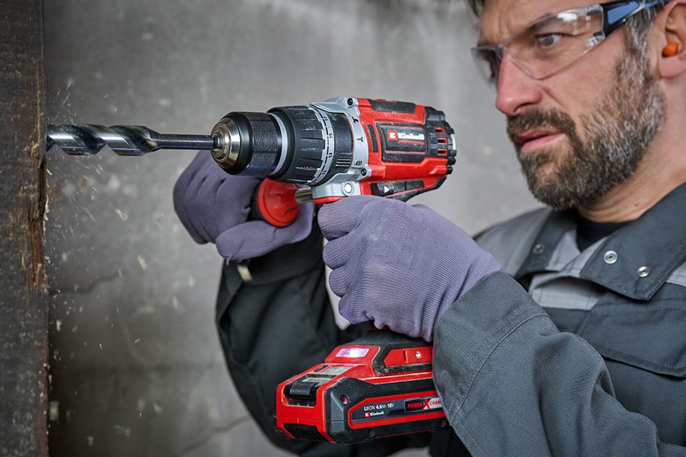 A man using Einhell red and black cordless drill against concrete.