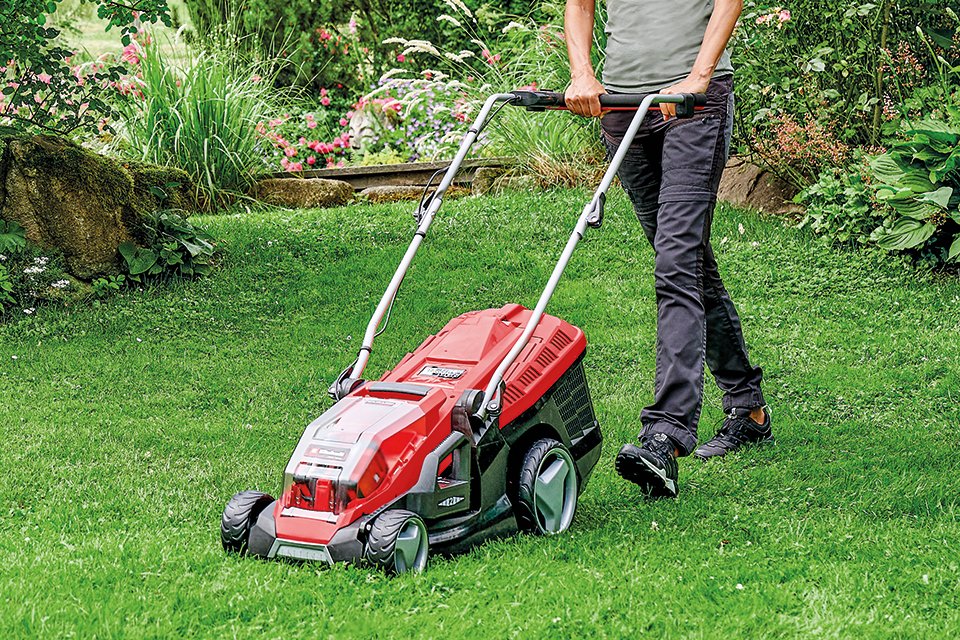 A person using Einhell cordless lawnmower on grass.
