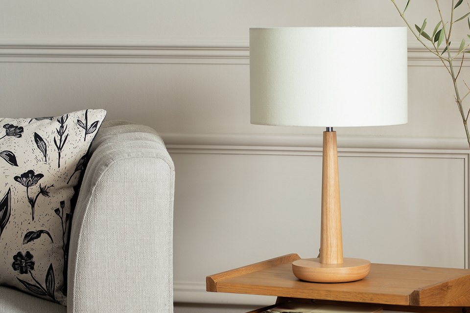 A Habitat walnut tapered wood table lamp in a room placed next to a white sofa.