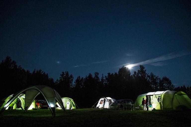 A campsite at nighttime showing four green tents and a gazebo.