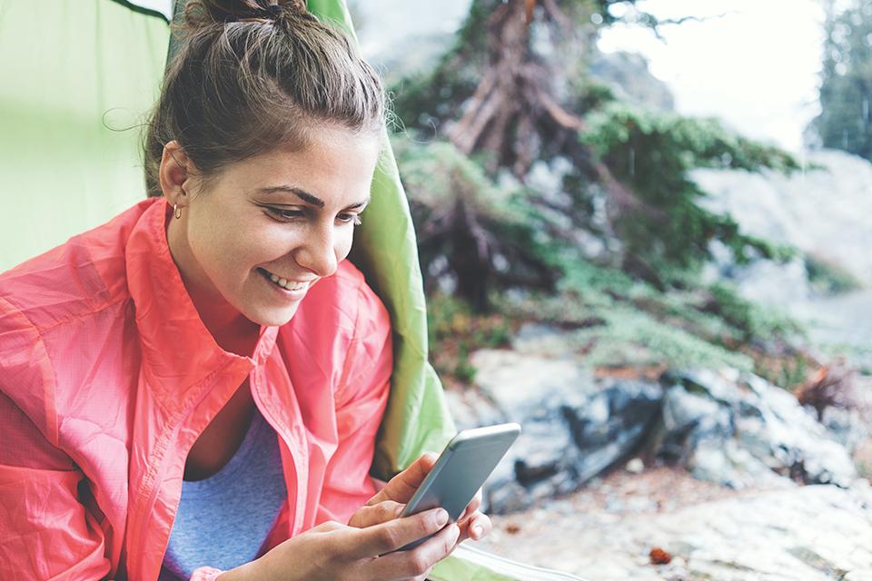Woman sat in a tent in a forest on her phone.
