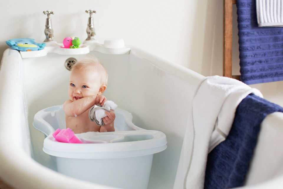 A baby having fun while bathing in the baby bath tub placed in a large bath tub.