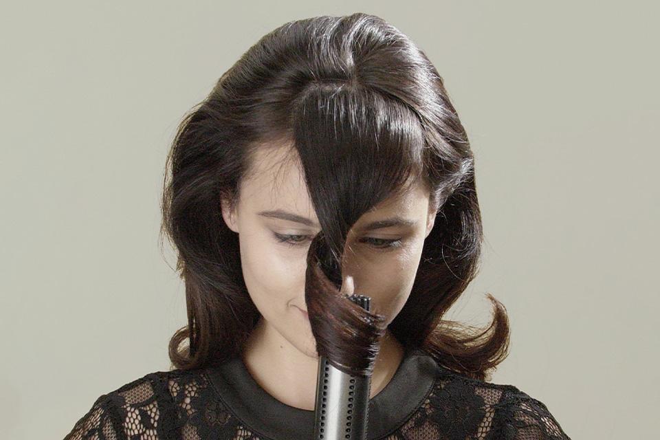 A brunette lady curling her hair with a styling brush.