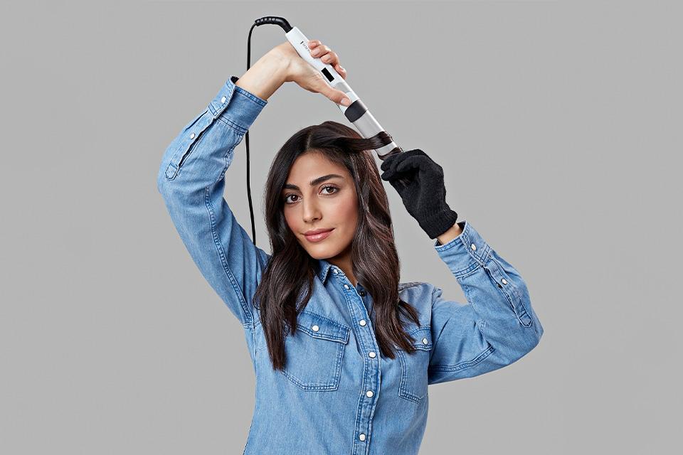 A lady using the Remington CI89H1 HYDRAluxe curing wand with a protective glove on.