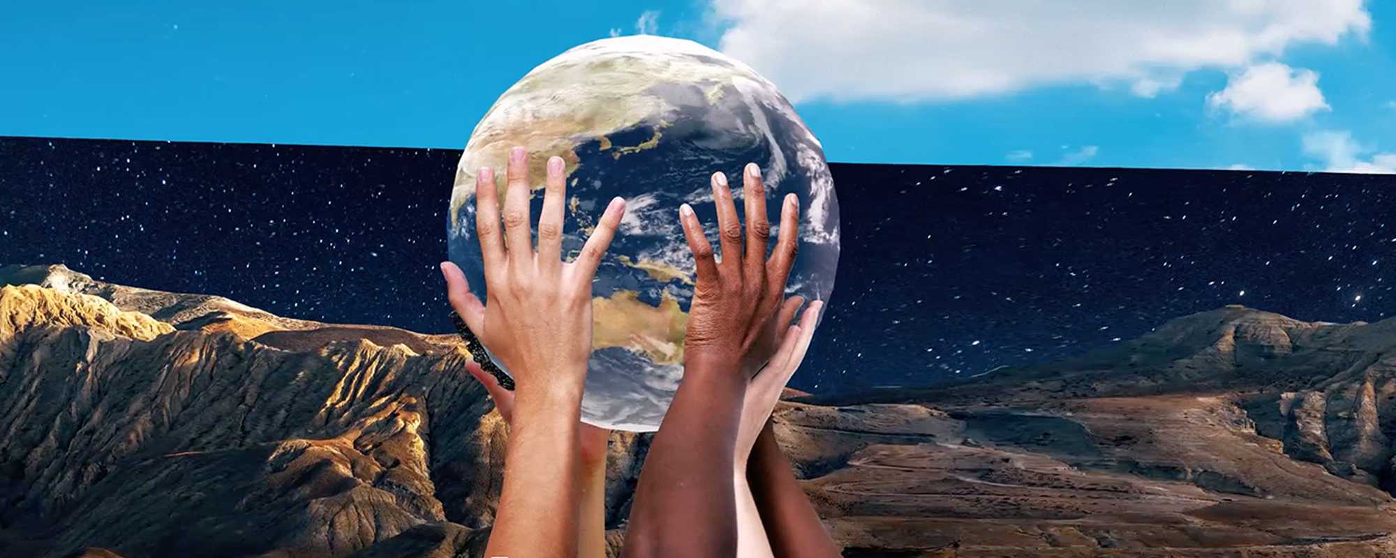 Image shows four human hands, all with different skin colours,  supporting a beach ball-sized globe. This is overlaid onto a composite background of blue sky, starry night sky, and dramatic mountains.