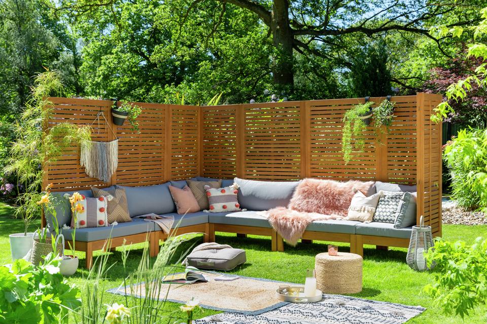A huge garden corner sofa set decorated with cushions and a woollen rug.
