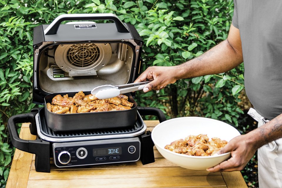 A man cooking outdoors using Ninja OG701UK Woodfire Electric BBQ Grill & Smoker.