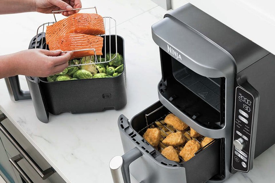A woman cooking multiple meals in a stackable Ninja air fryer. 