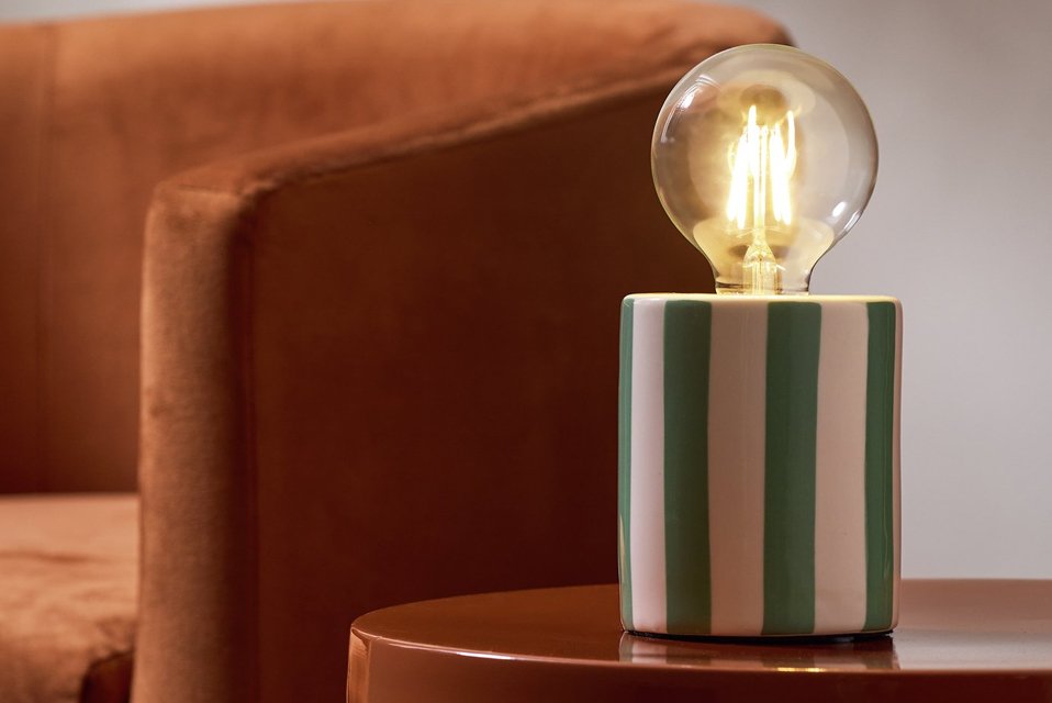 Green and white stripe lamp with large bulb on show on wooden side table.