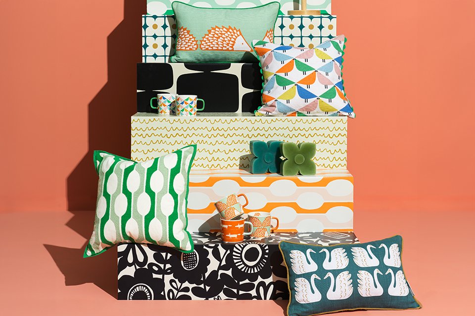Scion collaboration lamps, candles, cushions and mugsin bright colours and patterns stacked.