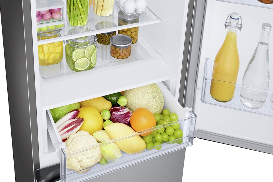Fresh fruits and vegetables along with bottles stored in the door and shelves of a Samsung freestanding fridge freezer.