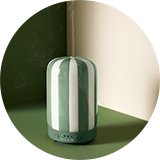 A Habitat diffuser with green and white stripes placed on a table.
