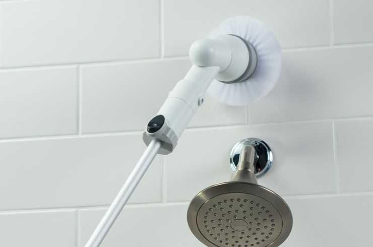 A scrubber being used to clean tiles around a shower head.