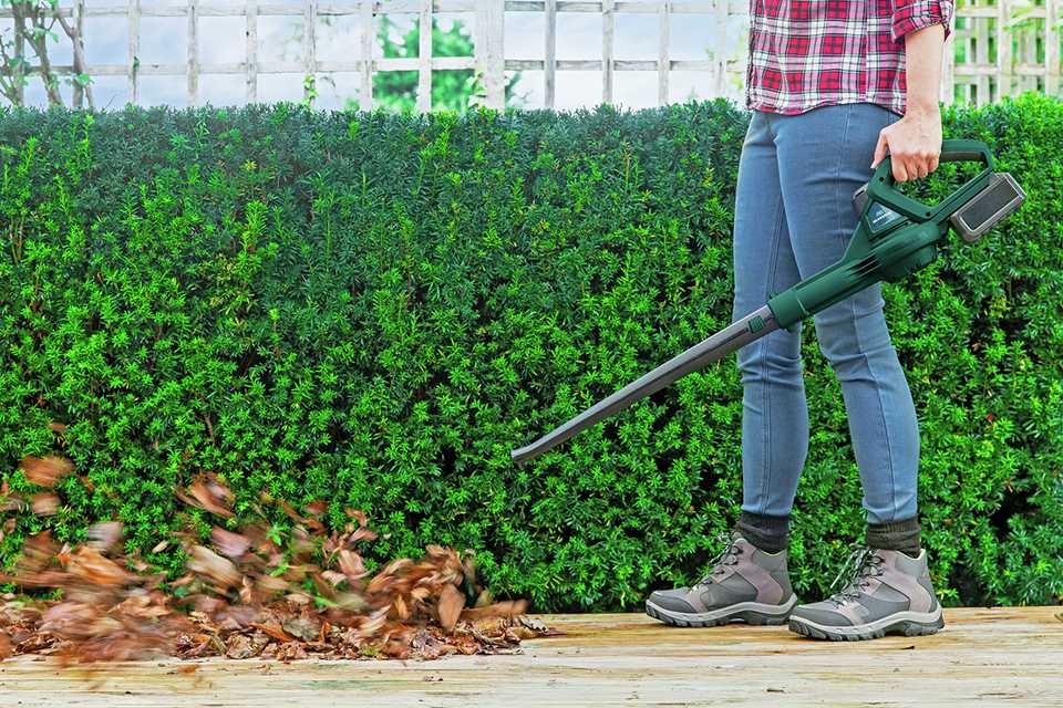 A person clearing away falled leaves with McGregor cordless leaf blower.