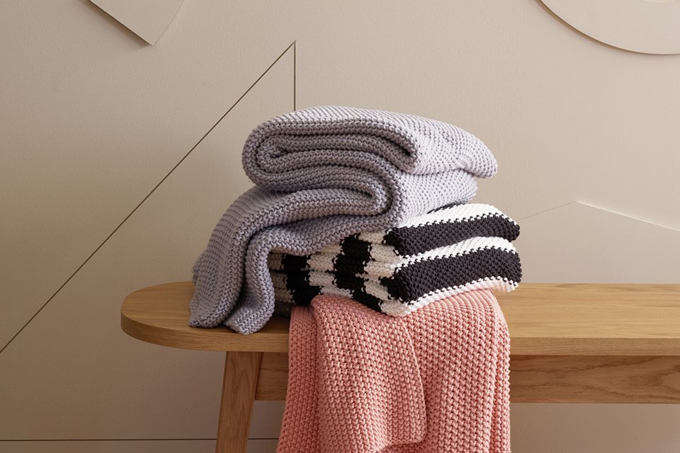 Blankets stacked on wooden bench.