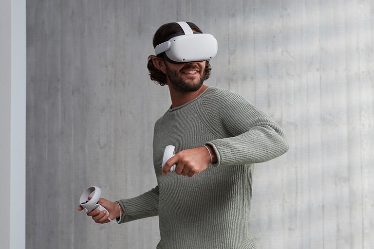 A smiling man in a grey top is shown using the Oculus Quest VR headset and controllers.